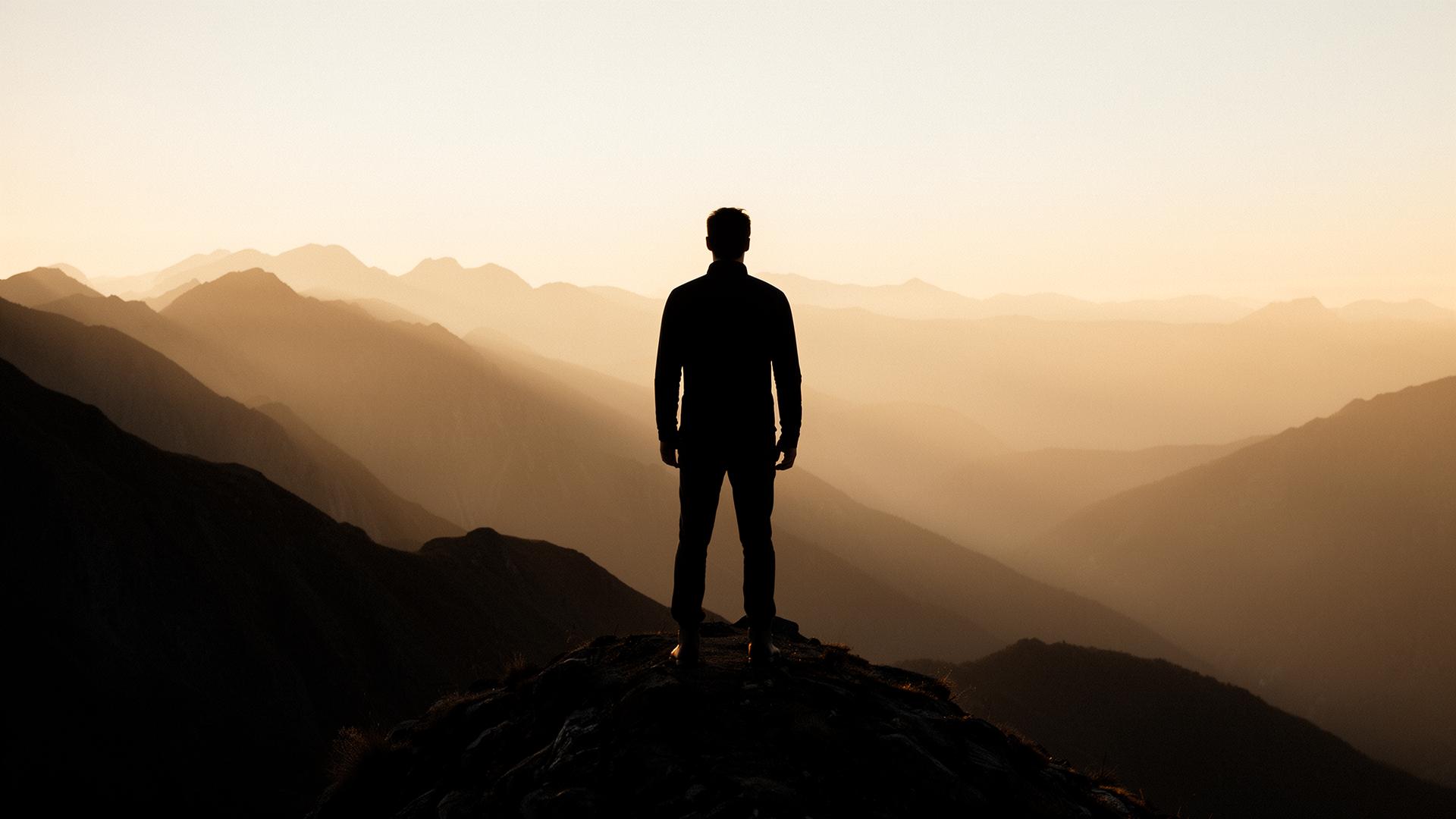 Silhouette d'aventurier face à des montagnes au lever du soleil